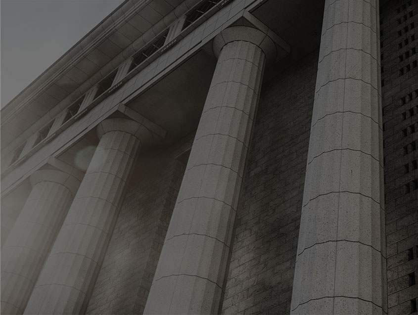 About us -A low-angle, desaturated view of the tall, neoclassical stone columns of a large, imposing building, possibly a courthouse or government building.