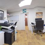 stepping stones office- A desk area is visible with a black roller blind covering a window, a computer setup, and a dark office chair.