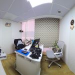 steppingstones office - A panoramic view of a small, bright private office featuring a white curved desk with two monitors, a white sofa on the left, and a geometric-patterned curtain on the back wall. The room has light wood flooring, textured walls, and a white door with a "PUSH" sign on the right.
