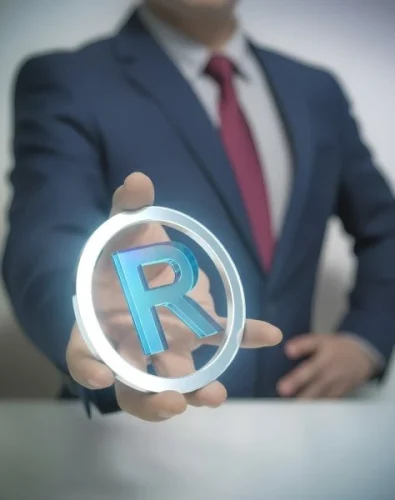 Trademark Registration - A man in a blue suit and red tie holds out a glowing, transparent circle containing a bright blue, three-dimensional registered trademark symbol (R), with the focus on the symbol.
