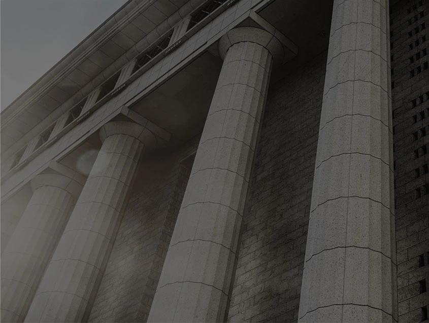 About us -A low-angle, desaturated view of the tall, neoclassical stone columns of a large, imposing building, possibly a courthouse or government building.